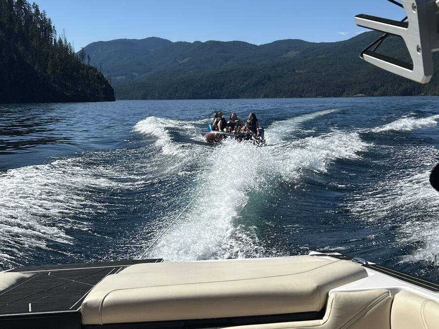 Getting towed on an inflatable tube behind a boat on Sproat Lake, with forested mountains along the shoreline