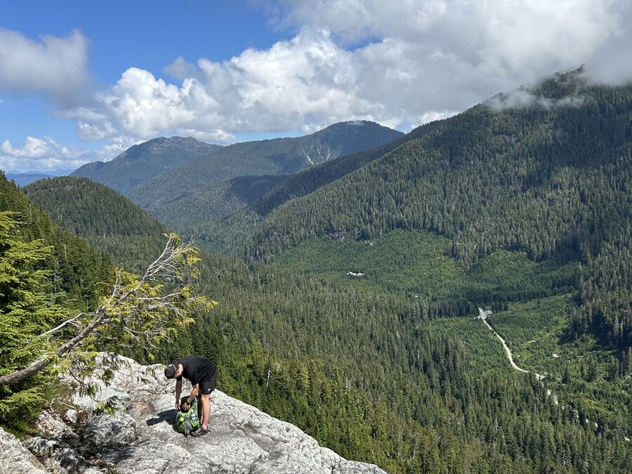 A hiker pausing on a rocky outcrop overlooking a forested valley on the Triple Peak trail